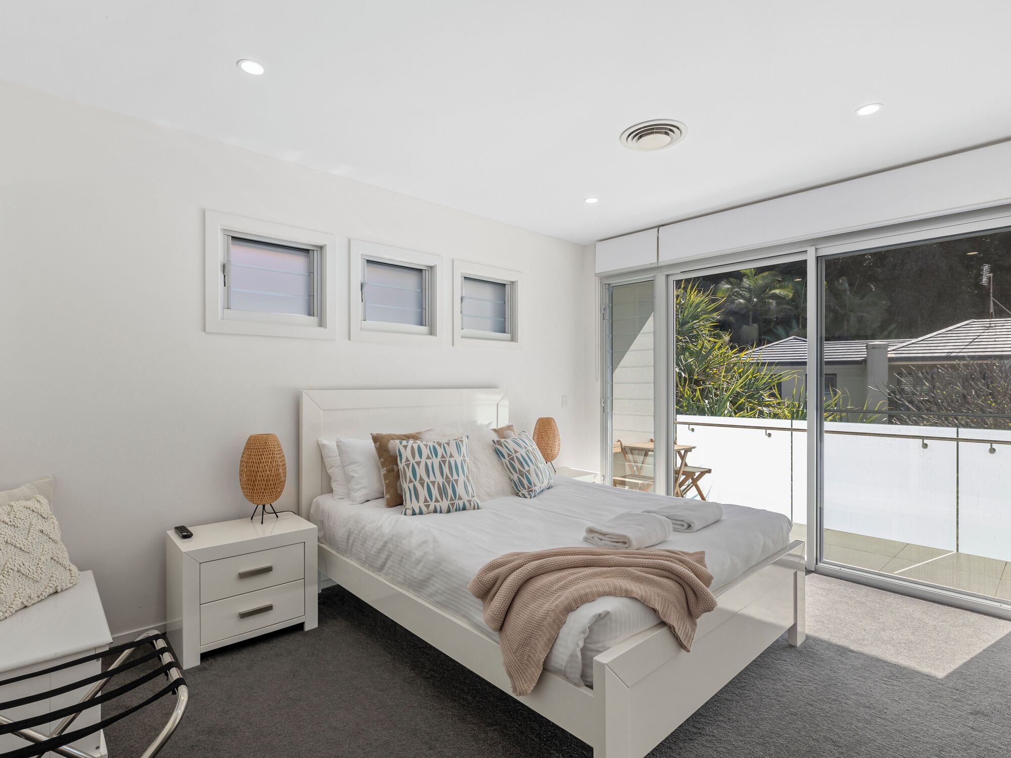A modern bedroom with a large bed, bedside tables, and a sliding glass door leading to an outdoor area.