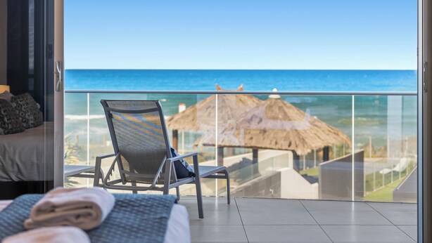 A balcony with a view of the ocean, a chair, and a bed with a view. - Beachfront #12 Beach Access, Pool, PetFriendly (Sapphire Beach)