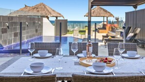A dining table set with white plates, bowls, and glasses, overlooking a pool with a view of the ocean. - Beachfront #12 Beach Access, Pool, PetFriendly (Sapphire Beach)