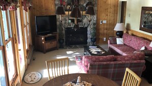 A cozy living room with a fireplace, wooden beams, a stone wall, a television, and a dining area with a table and chairs.
