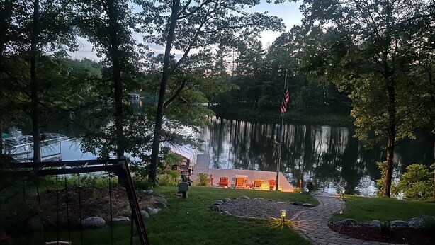 A serene lakeside setting with a swing set, a flag, and a well-maintained garden path.