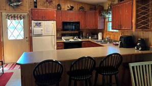 A kitchen with wooden cabinets, a refrigerator, a microwave, a stove, and a sink. There are three chairs at the counter.