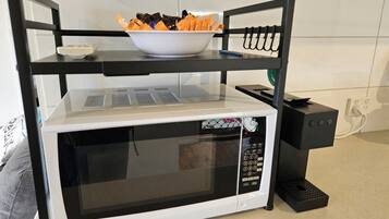 A kitchen with a microwave on a black stand, a bowl of snacks on top, and a power outlet on the wall.