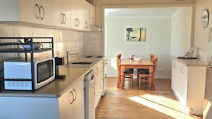 A kitchen with white cabinets, a microwave, and a dining area with a wooden table and chairs. - Relax at Red Rocks - Pet friendly- WiFi - Winter special 4th night free (Cowes)