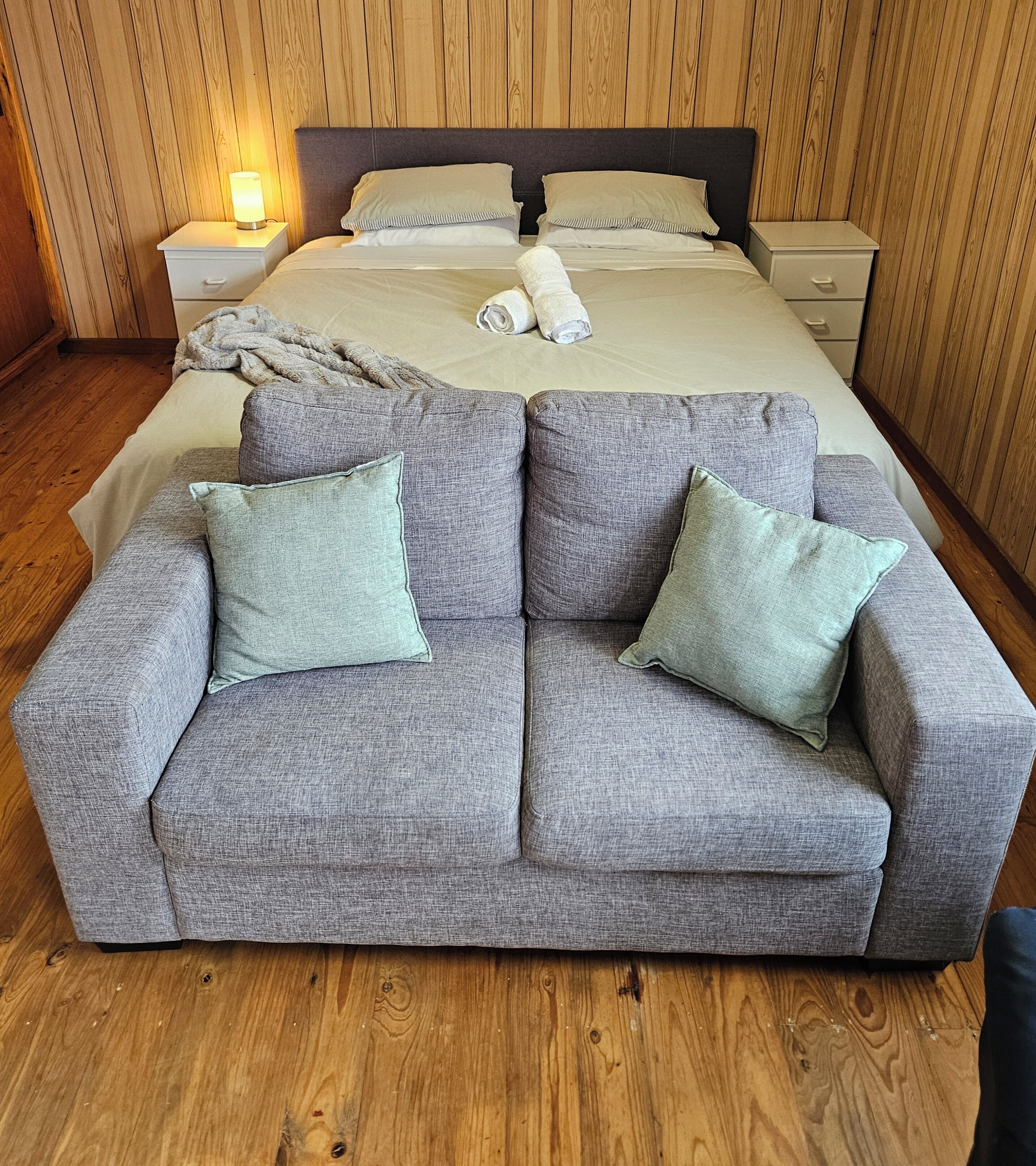 Une chambre à coucher avec un lit, deux tables de chevet, un canapé gris avec des coussins et un plancher en bois.