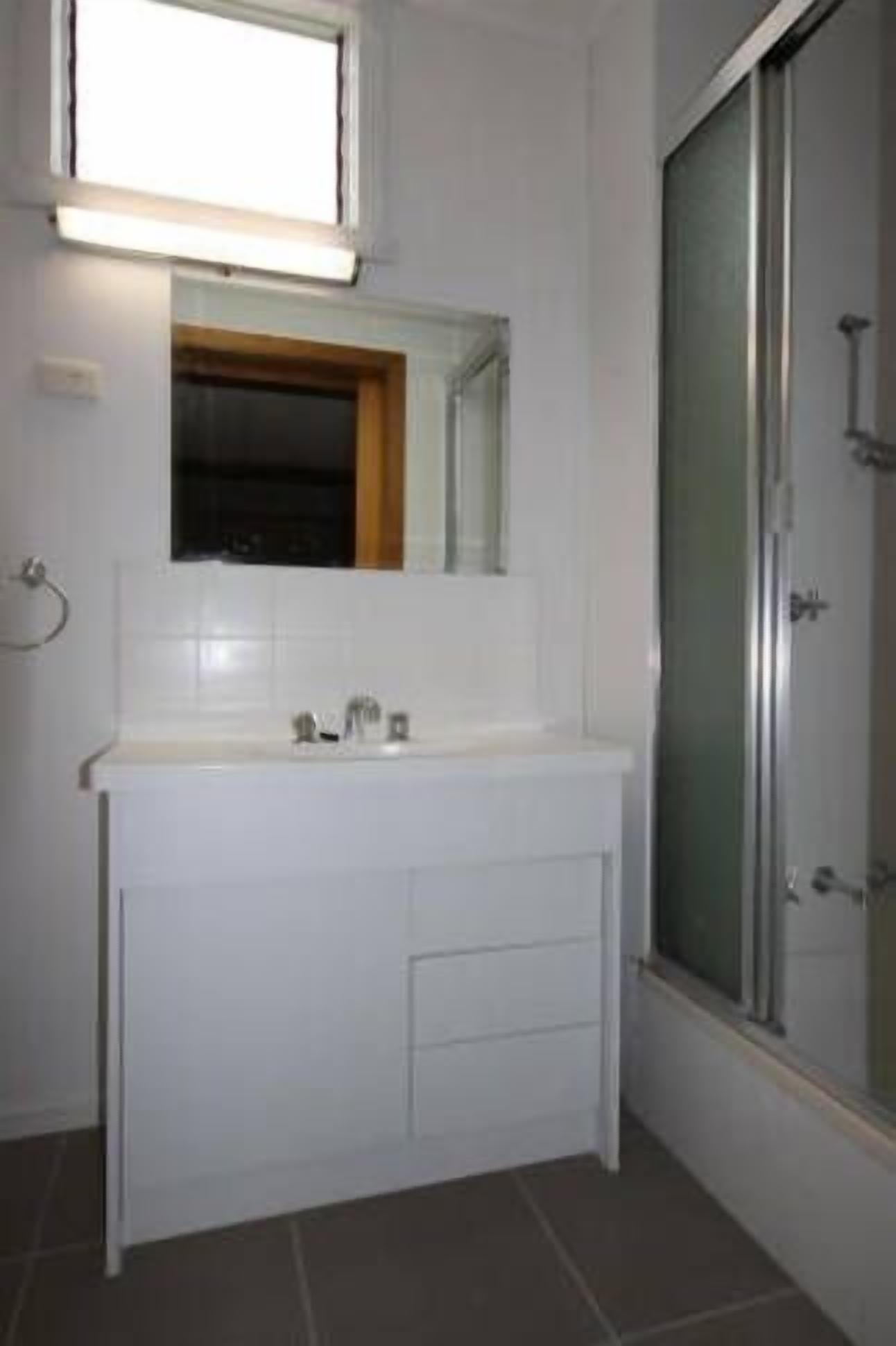 Une salle de bain avec un meuble-lavabo blanc, un miroir au-dessus du lavabo et un espace douche doté d’une porte en verre.