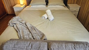 A neatly made bed with a blanket and rolled towels, wooden panel walls, a nightstand with a lamp, and a dresser with drawers. - Relax at Red Rocks - Pet friendly- WiFi - Winter special 4th night free (Cowes)