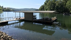 A dock with a covered seating area and a small building, surrounded by calm water and trees. - Czarnecky Home - Waterfront Home in Deerfield Resort, Dock, Hot Tub, Firepit (La Follette)