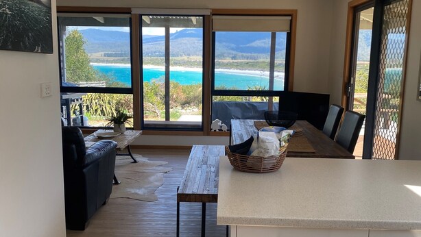 A modern living room with a wooden floor, a black sofa, a wooden table, and a view of the ocean through large windows. - WOW! No better location.
Beachfront, private & tranquil. Unwind and reconnect... (Seymour)