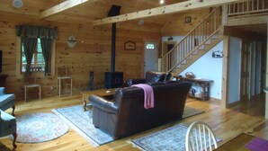 A cozy cabin interior with a wooden interior, a leather sofa, a staircase, and a fireplace.