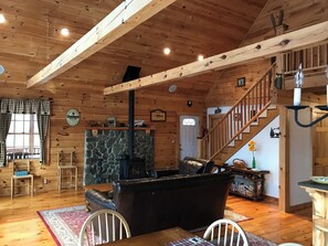 A wooden interior with a stone fireplace, a staircase, and a dining area.
