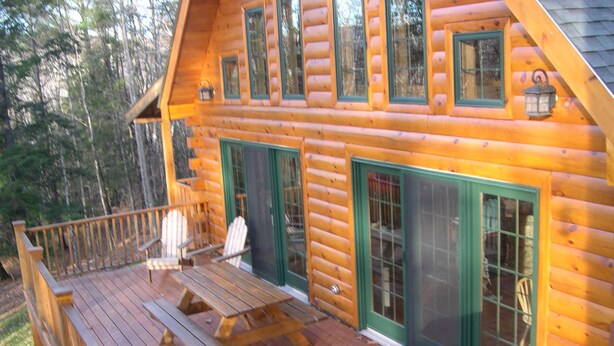 A log cabin with a deck, outdoor seating, and a grill.