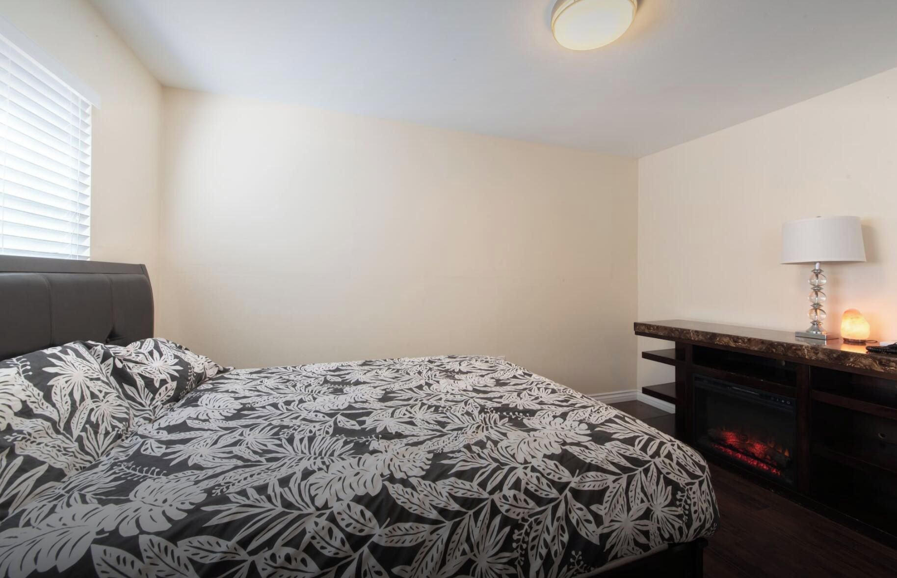 A bedroom with a bed, a nightstand, a lamp, and a fireplace.