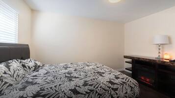 A bedroom with a bed, a nightstand, a lamp, and a fireplace.