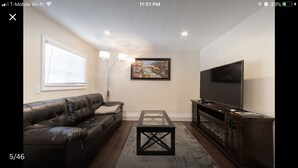 A living room with a leather sofa, a glass coffee table, a TV on a wooden stand, and a painting on the wall. - Private Guest house close to Disneyland & Little Saigon Mall (Santa Ana)