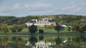 A large, white, multi-story building with a symmetrical facade, situated on a hill with a lake in the foreground reflecting the building. - Private Beach & Pier Lake Front w/ Fireplace on Lake Como - Walk to Mars Resort! (Lake Geneva)