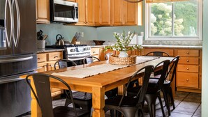 A kitchen with wooden cabinets, stainless steel appliances, a dining table with chairs, and a window with a view of trees. - Private Beach & Pier Lake Front w/ Fireplace on Lake Como - Walk to Mars Resort! (Lake Geneva)