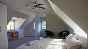 Ein Schlafzimmer mit einem großen Bett, einem Schreibtisch, zwei Stühlen und einem Deckenventilator.