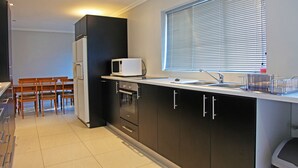 Eine moderne Küche mit dunklen Schränken, einer weißen Arbeitsplatte, einer Mikrowelle, einem Spülbecken und einem Fenster mit Jalousien.