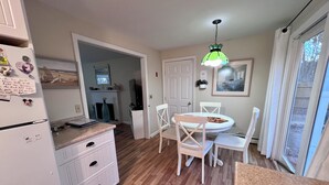 A compact kitchen with a dining area, wooden flooring, white cabinetry, a small refrigerator, and a green pendant light. - Quiet 3BR Ranch - Little Dog Friendly! (2033) (Harwich)