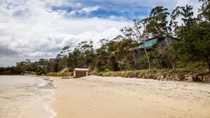 Ein Strand mit einer Holzkonstruktion, einem modernen Gebäude und dichter Bepflanzung.