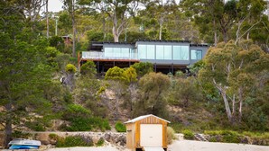 Ein modernes Haus mit Glasfassade, einer Holzsteganlage und einer Strandlage.