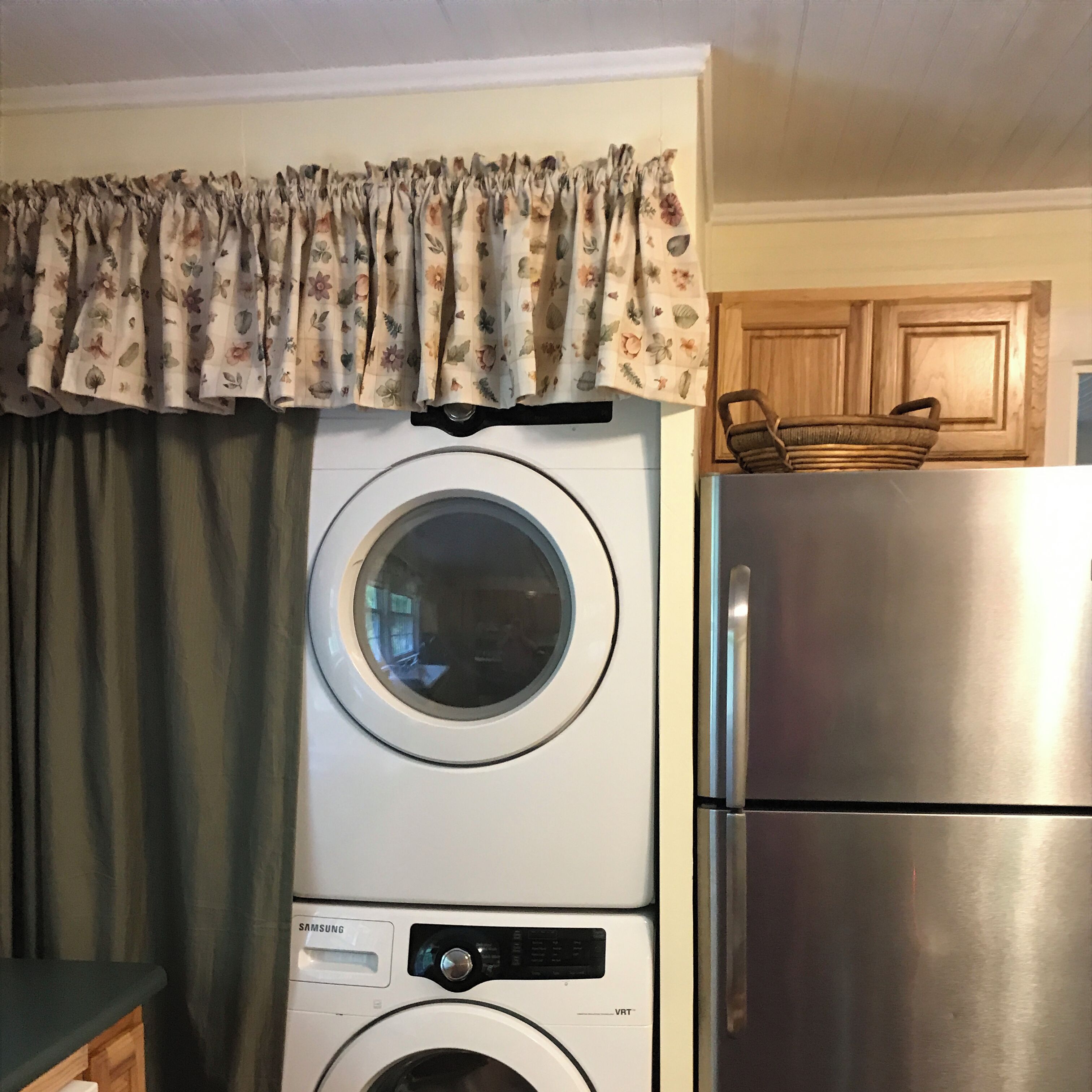 A compact laundry area with a front-loading washing machine, a stainless steel refrigerator, and a wooden cabinet.