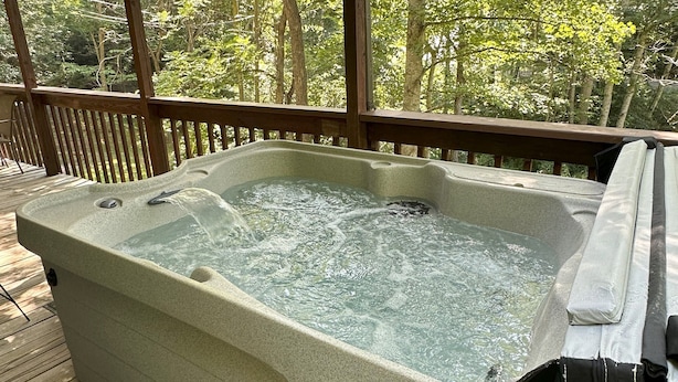 A hot tub on a wooden deck with a view of a forest.