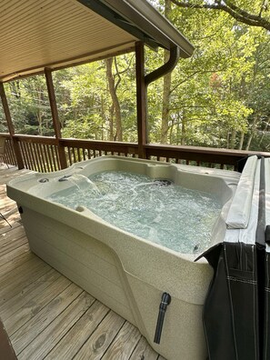 Ein Whirlpool auf einer Holzterrasse mit Blick auf einen Wald.