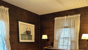 A wooden-paneled bedroom with a bed, two bedside lamps, a framed picture, and a window with curtains.