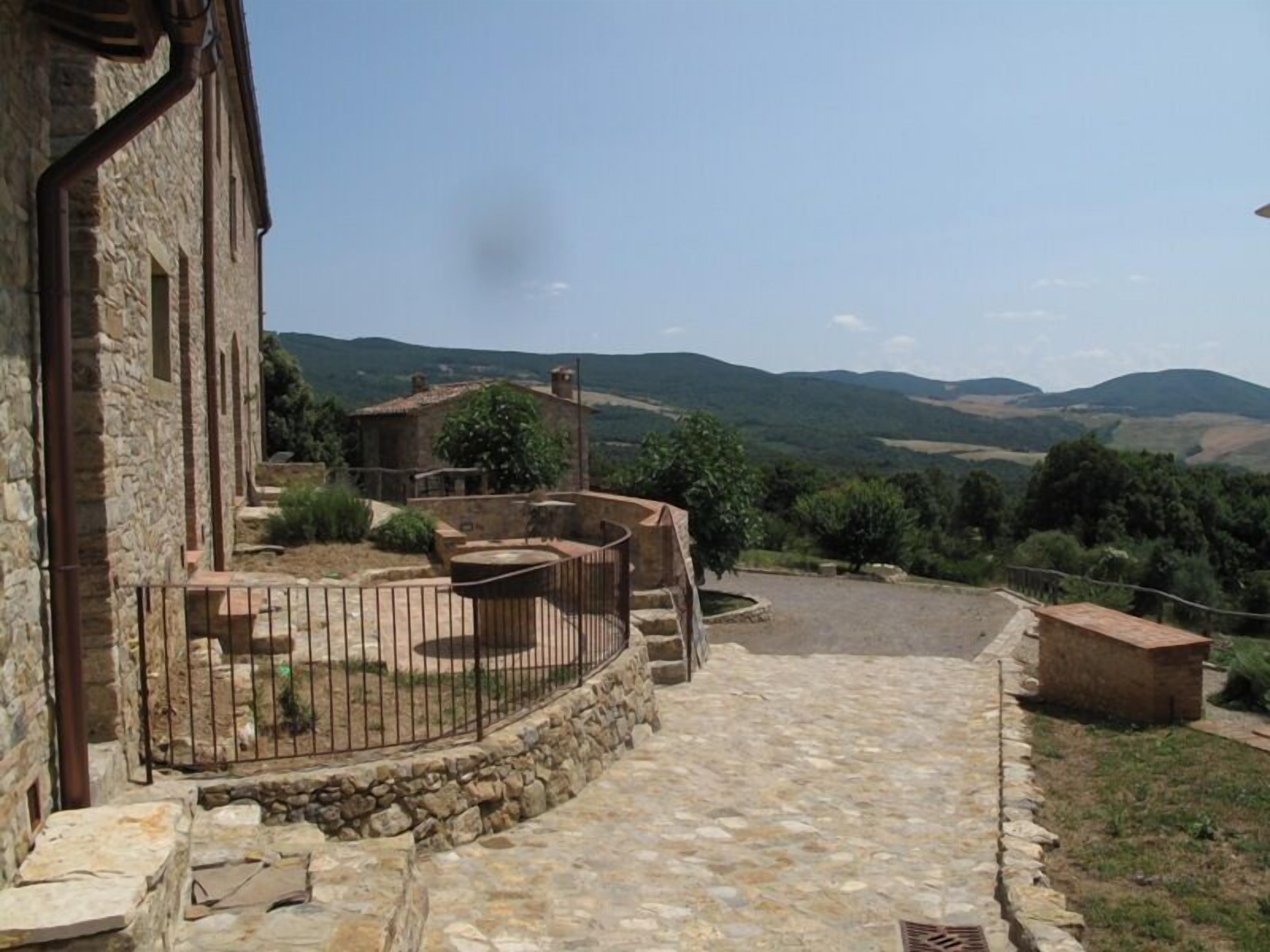 A stone building with a stone pathway leading to a fenced outdoor area with a view of rolling hills.