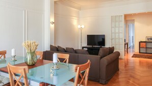 Ett modernt vardagsrum med ett matbord i glas, en brun soffa och en platt-TV.