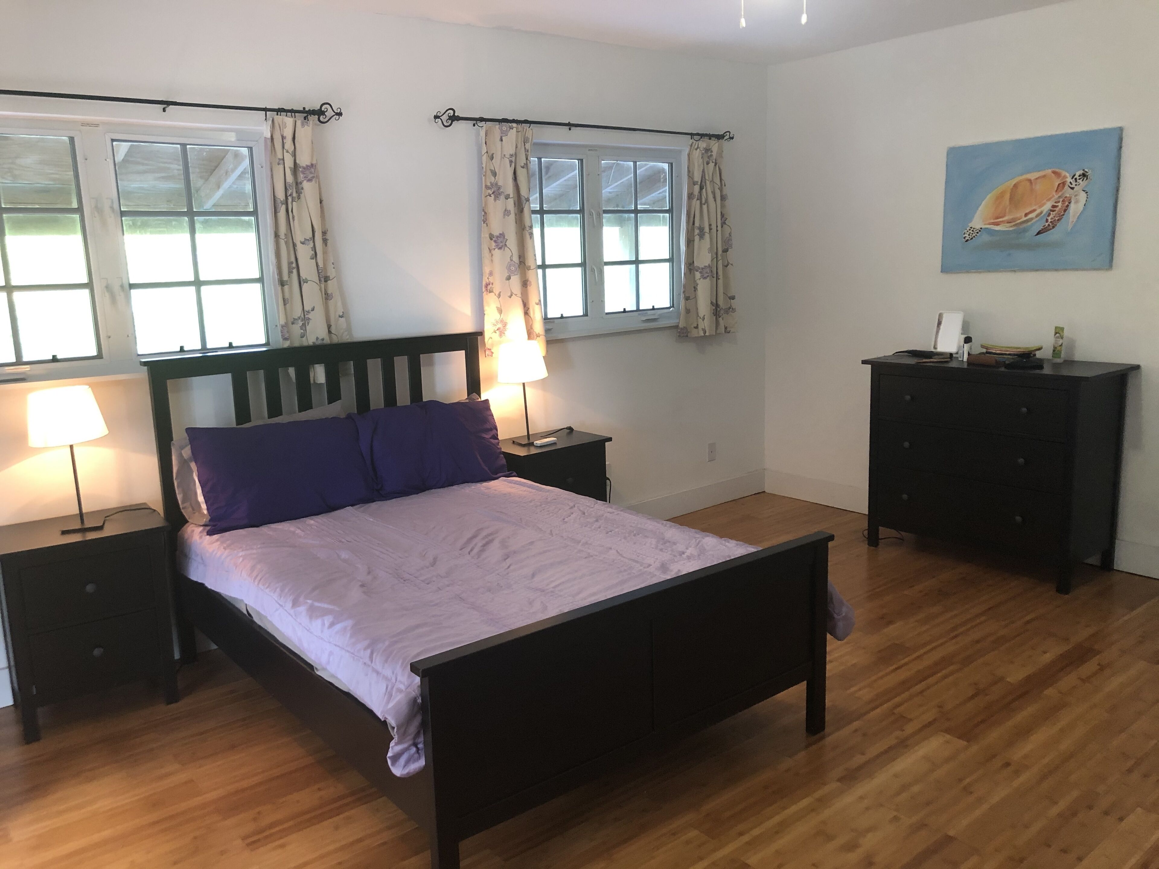 A bedroom with a bed, two bedside tables, a dresser, and a window with curtains.