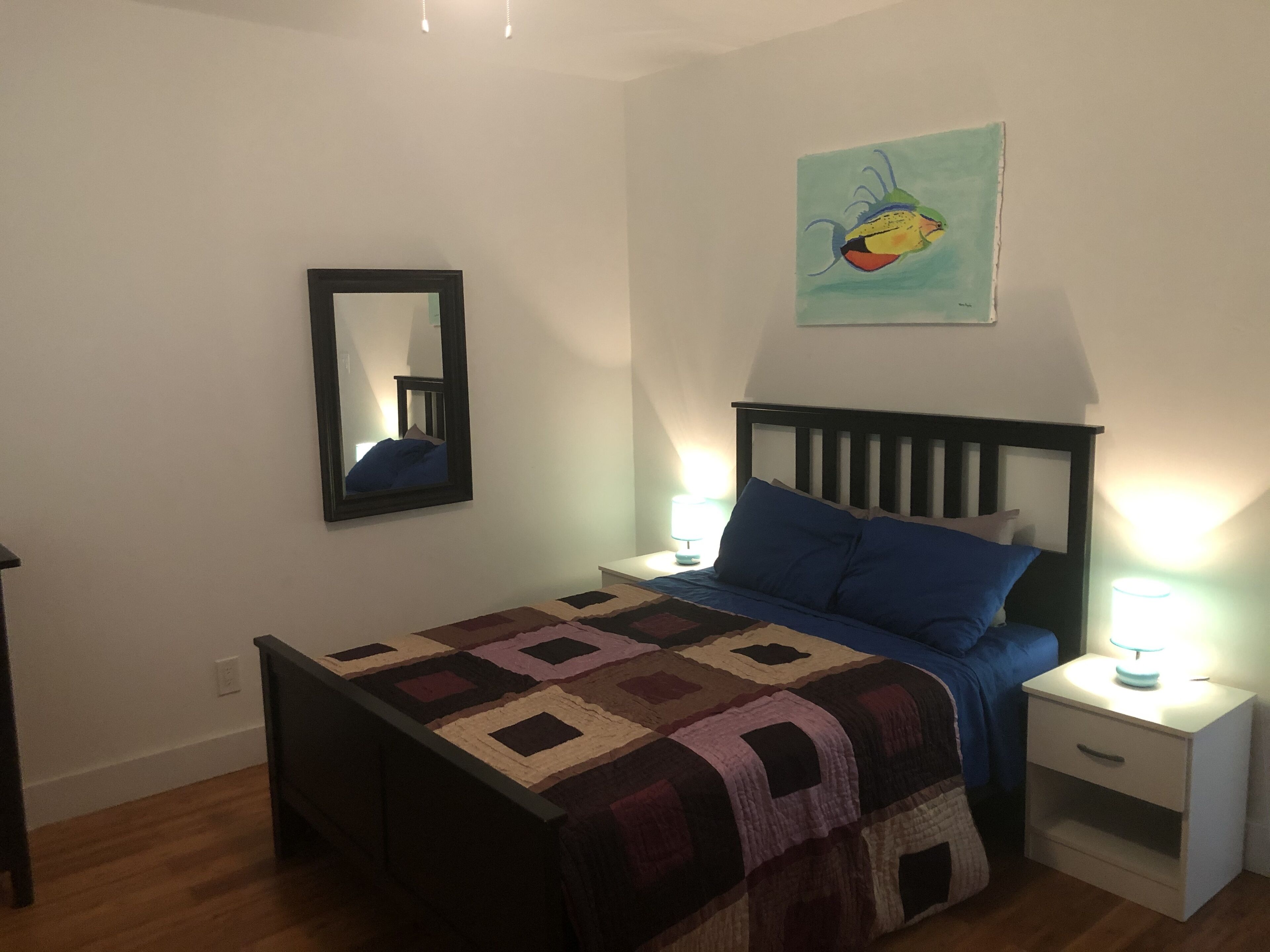 A bedroom with a bed, a nightstand, a bedside lamp, a mirror, and a painting on the wall.