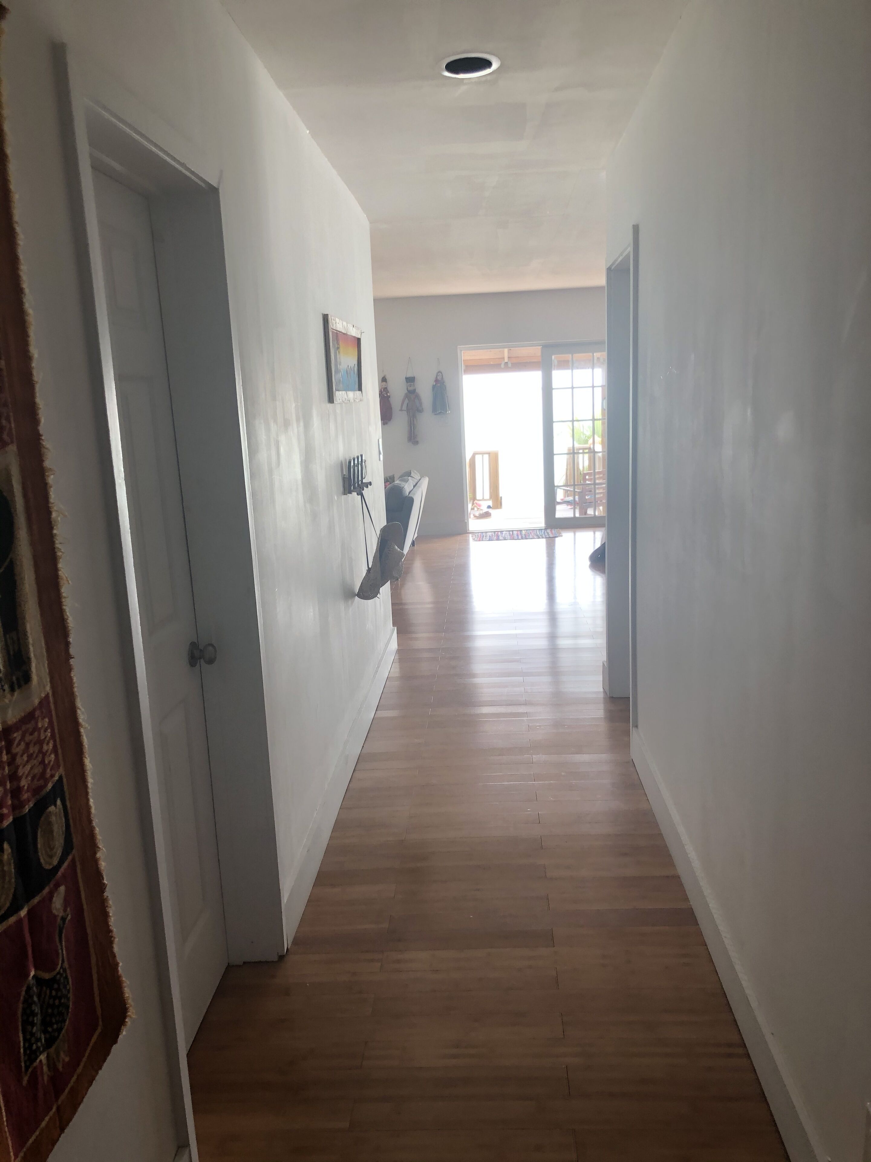 A hallway with wooden flooring, white walls, and a door on the left.