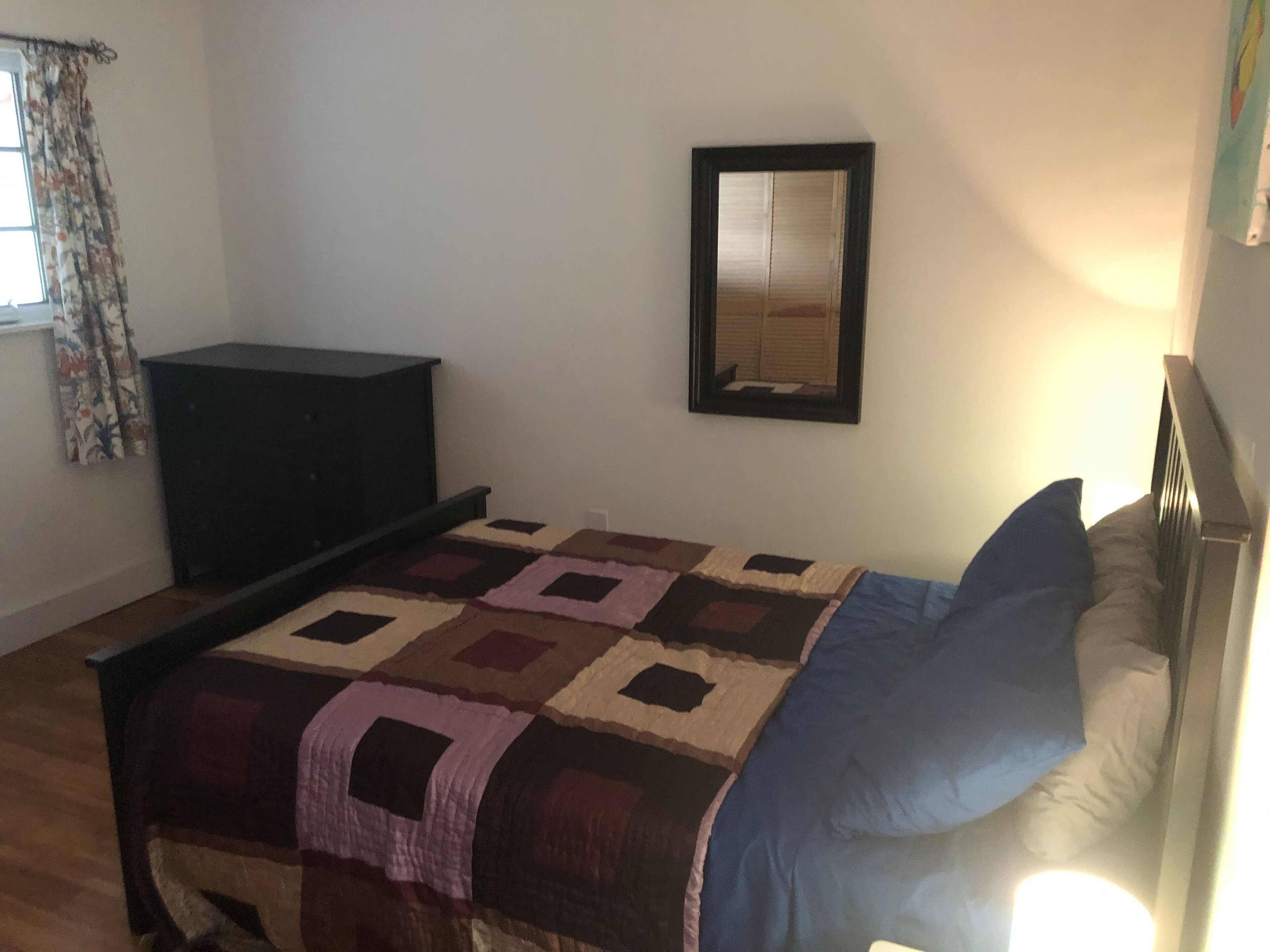 Un dormitorio con cama, cómoda, espejo y ventana con cortinas.