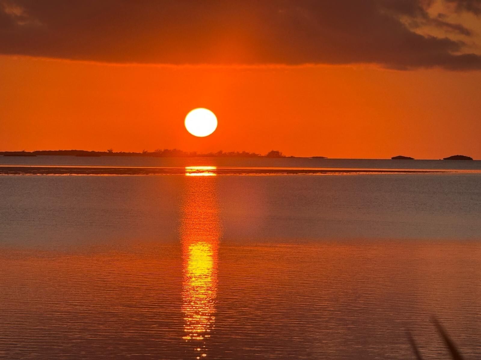 A sunset over a calm body of water with a visible reflection of the sun.