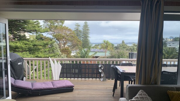 A covered outdoor area with a wooden deck, a cushioned seating area, a table, and a sofa. - Teaghlach: Tapeka / Russell Holiday Home (Tapeka Point (Russell))
