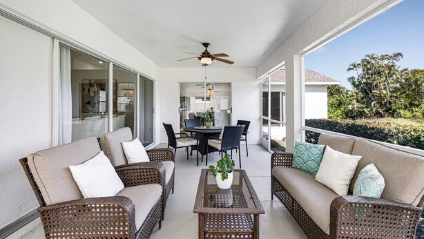 Une terrasse extérieure couverte, aménagée avec des meubles en osier, un ventilateur de plafond et un coin repas comprenant des chaises et une table.