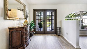 Un couloir avec une armoire en bois, un miroir et une porte donnant sur l’extérieur.