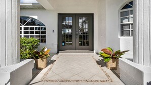 Une entrée de maison avec un chemin dallé, deux plantes en pot et une porte à deux battants.