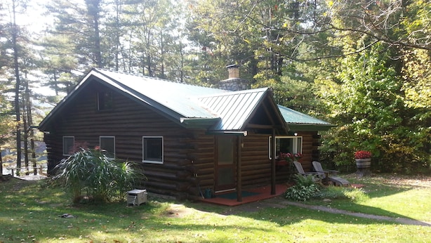 A log cabin with a green roof, surrounded by trees and a grassy yard. - Adirondack Lakeside Log Cabin With Mountain Views (Mountain View)