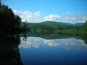 A calm lake reflecting trees and a mountain range. - Adirondack Lakeside Log Cabin With Mountain Views (Mountain View)