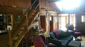 A cozy log cabin interior with a wooden staircase, a sofa, a table, and a lamp. - Adirondack Lakeside Log Cabin With Mountain Views (Mountain View)