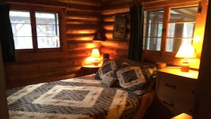 A cozy log cabin bedroom with a bed, two bedside lamps, a dresser, and a window with curtains. - Adirondack Lakeside Log Cabin With Mountain Views (Mountain View)