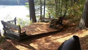 A wooden deck with benches overlooking a lake, surrounded by trees. - Adirondack Lakeside Log Cabin With Mountain Views (Mountain View)