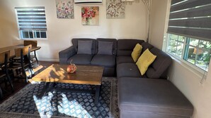 Una sala de estar con un sofá modular, una mesa de centro de madera, un tapete estampado y un comedor con una mesa y sillas.