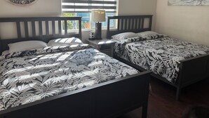 Un dormitorio con dos camas, una ventana con persianas, una mesita de noche con lámpara y una obra de arte en la pared.