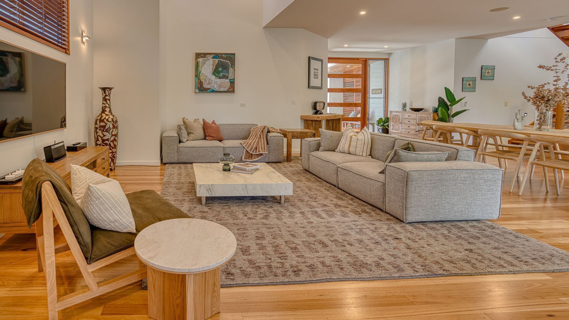 A modern living room with a grey sofa set, a coffee table, and a dining area with wooden furniture.
