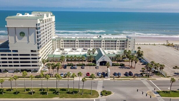 A hotel with a beach view, multiple parking lots, and a prominent tower. - Beautiful 9th floor OceanView Studio Condo  - Pool is OPEN! (Daytona Beach)